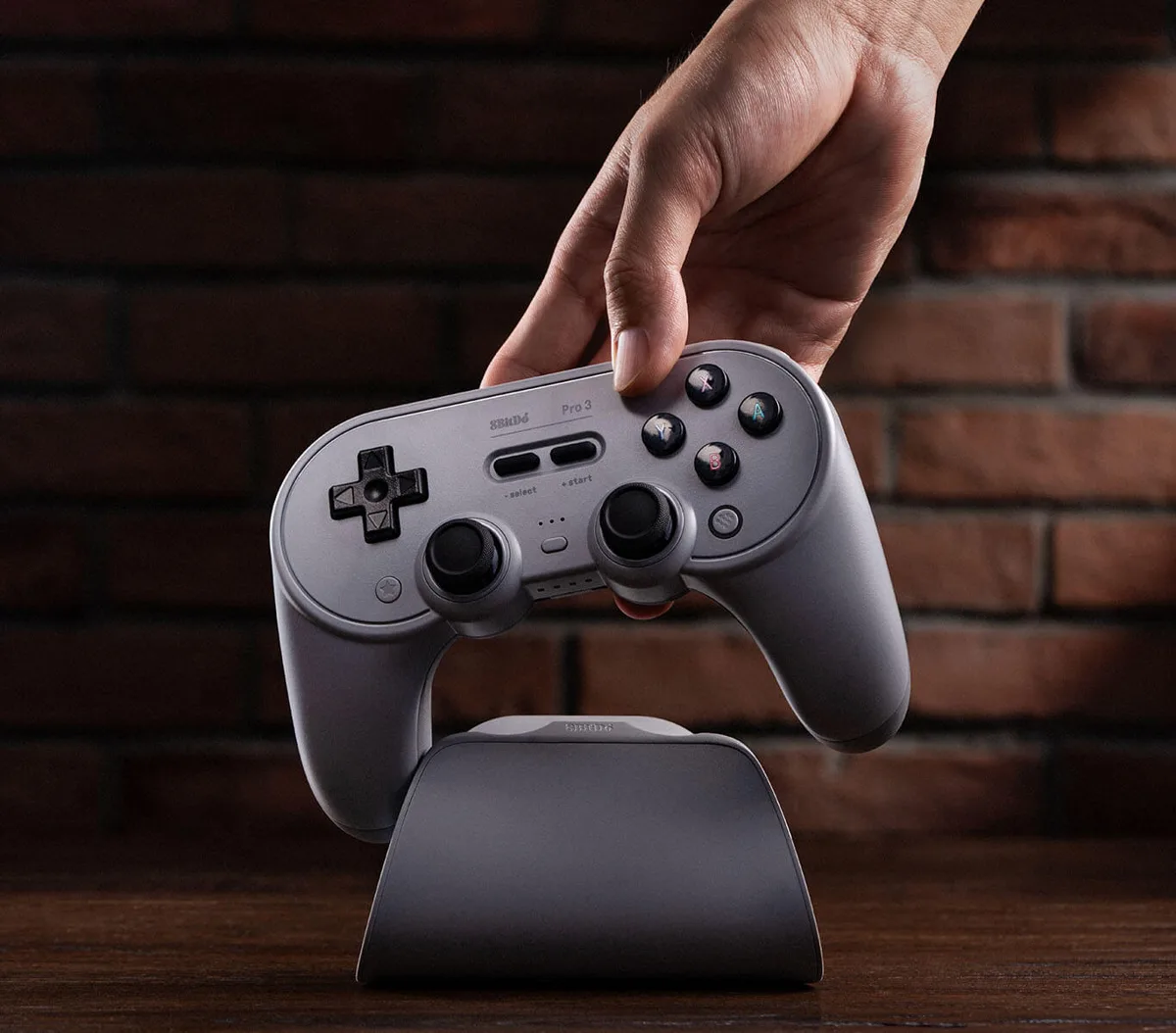 Hand lifting a gray 8BitDo Pro 3 off its charging dock
