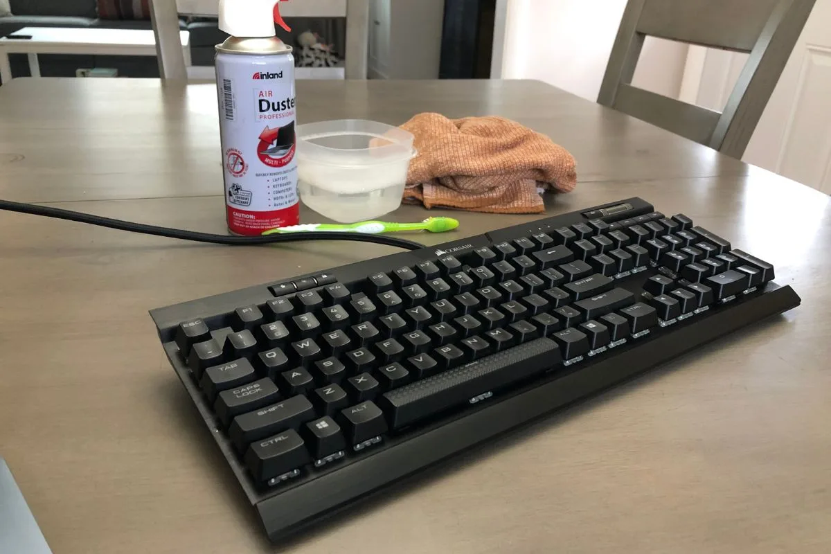 Unplugged mechanical keyboard with compressed air, a toothbrush, a bowl and a cloth ready for cleaning