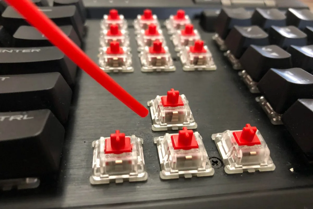 Compressed air straw nozzle blowing dust from exposed mechanical keyboard switches