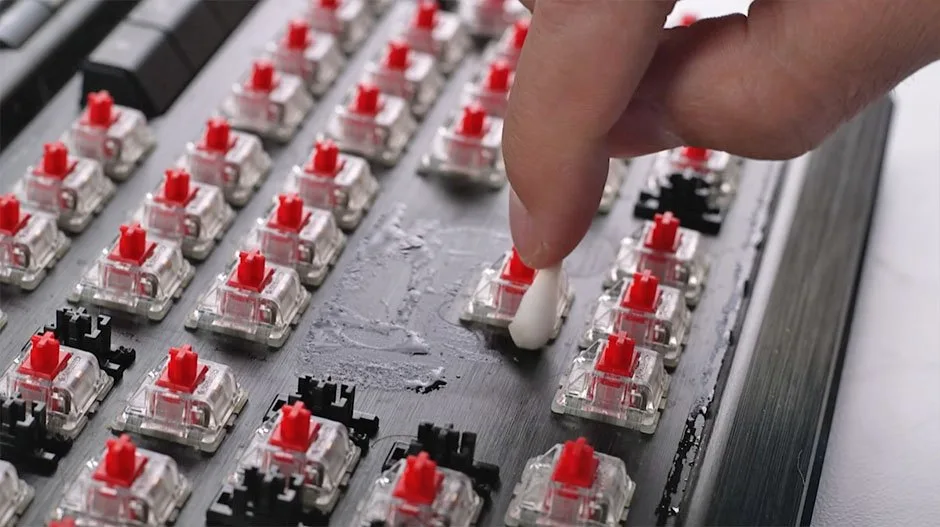 Cotton swab dipped in isopropyl alcohol cleaning the keyboard plate around switches