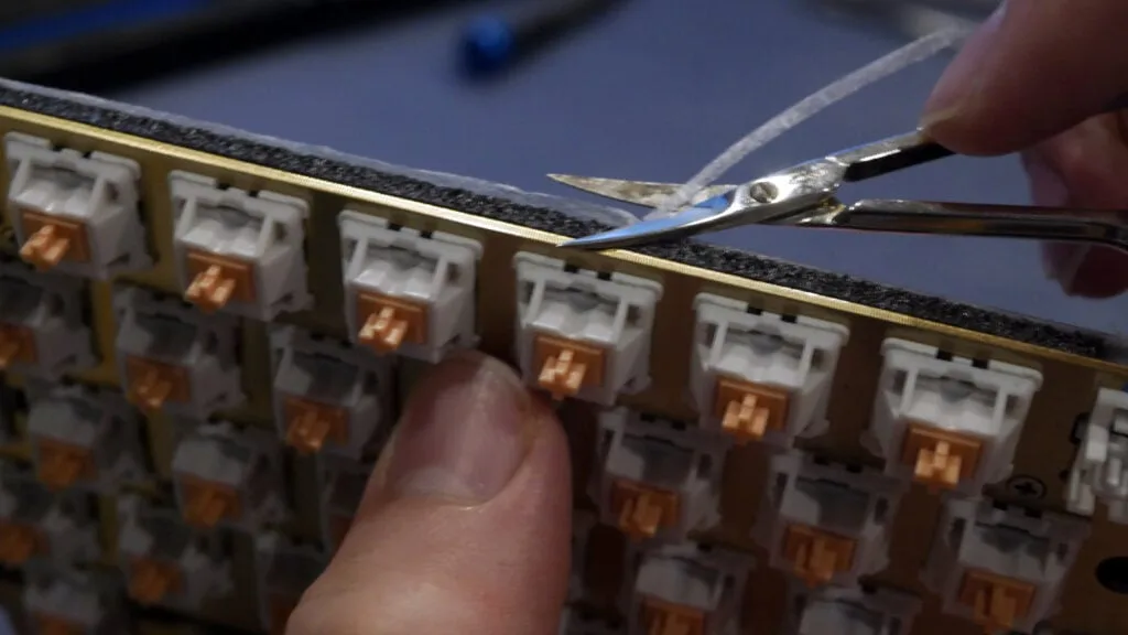 Scissors trimming excess PE foam from the edge of the keyboard PCB