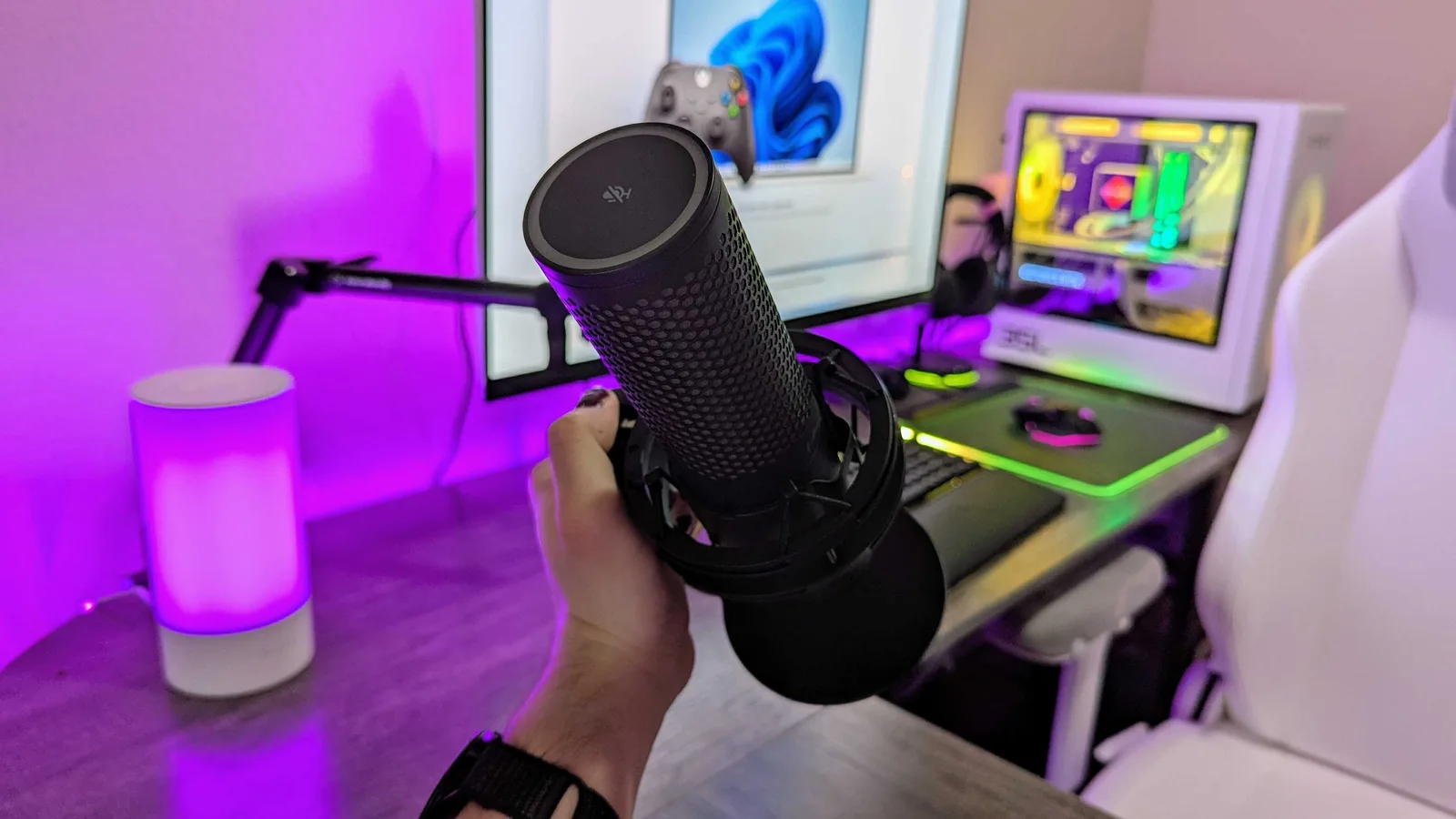 QuadCast 2 S USB mic held in front of a gaming desk setup