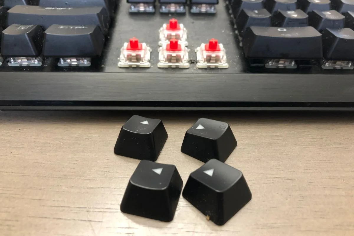 Arrow keycaps removed from a mechanical keyboard with red switches exposed