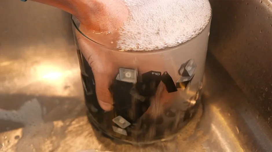 Keycaps being rinsed in a glass of water at the sink to wash off soap