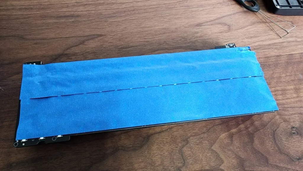 First layer of blue painter's tape applied across the back of a keyboard PCB