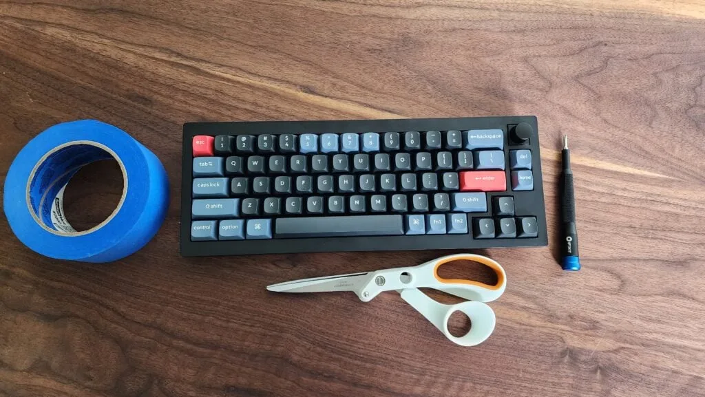 Painter's tape, scissors and a precision screwdriver next to a 65% keyboard for a tape mod