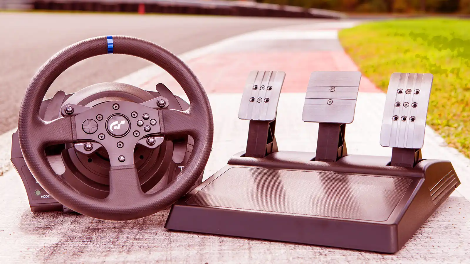 Thrustmaster T300RS GT racing wheel and three metal-faced pedals on a racetrack curb