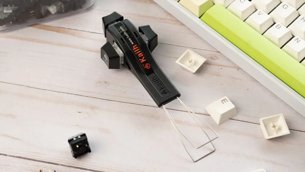 Wire keycap puller beside removed white keycaps on a mechanical keyboard