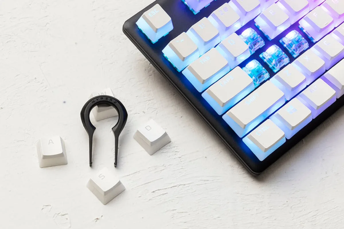 Keycap puller next to removed keycaps on a desk beside a keyboard