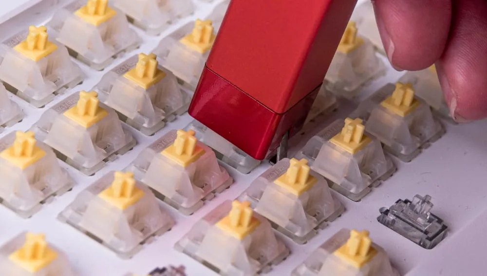 Red switch puller lifting a yellow-stem switch out of a hot-swappable keyboard
