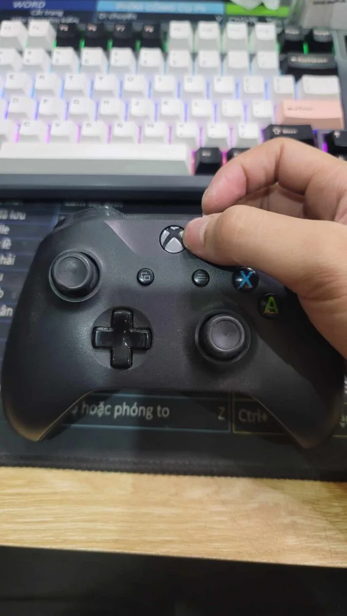 Hand pressing the Xbox button on top of an Xbox controller to turn it on